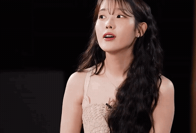 A Woman With Long Hair And A Necklace Looks At The Camera GIF