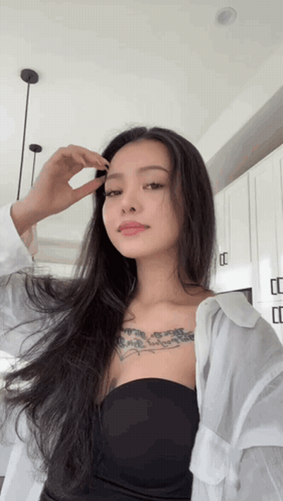 A Woman With Long Hair And A Tattoo On Her Chest Looks At The Camera GIF