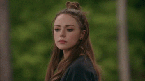 A Woman With Long Hair In A Bun Looks At The Camera GIF