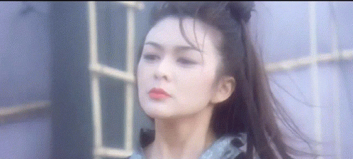 A Woman With Long Hair In A Ponytail Is Standing In Front Of A Window . GIF