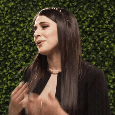 A Woman With Long Hair Is Clapping Her Hands In Front Of A Green Wall GIF