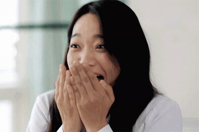 A Woman With Long Hair Is Covering Her Mouth With Her Hands . GIF