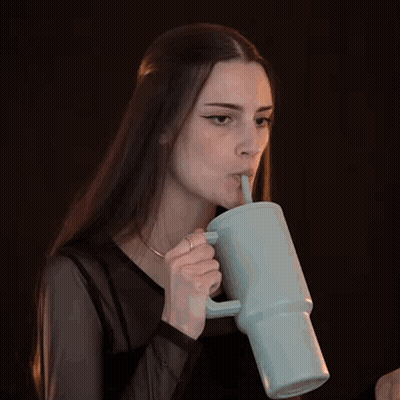 a woman with long hair is drinking from a mug with a straw .