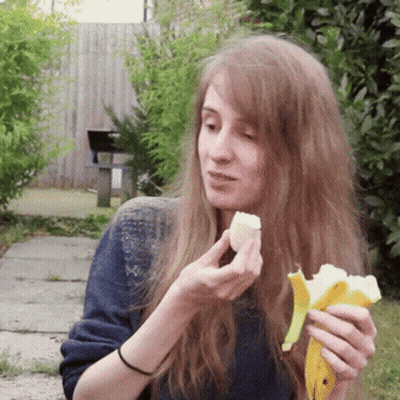 A Woman With Long Hair Is Eating A Banana Peel GIF
