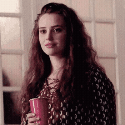 A Woman With Long Hair Is Holding A Red Cup In Her Hand And Looking At The Camera . GIF