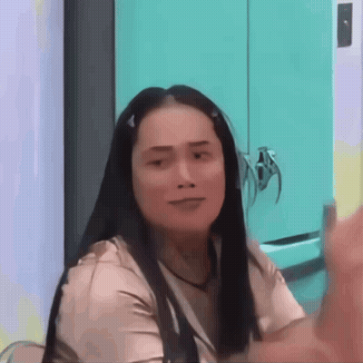 A Woman With Long Hair Is Sitting In Front Of A Blue Cabinet And Making A Funny Face . GIF