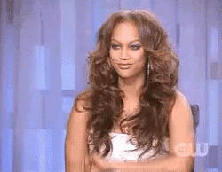 A Woman With Long Hair Is Sitting In Front Of A Curtain With The Word Cw On It GIF