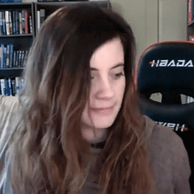 A Woman With Long Hair Is Sitting In Front Of A Gaming Chair And Making A Funny Face . GIF