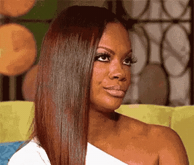 A Woman With Long Hair Is Sitting On A Couch And Looking At The Camera GIF