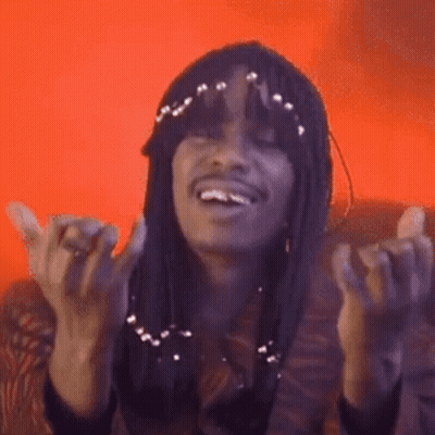 A Woman With Long Hair Is Sitting On A Couch With Her Hands In The Air And Smiling . GIF