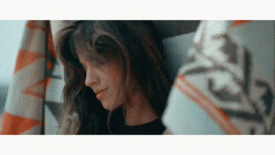 A Woman With Long Hair Is Sitting Under A Blanket And Smiling . GIF