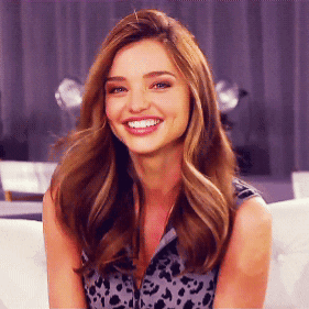 A Woman With Long Hair Is Smiling And Wearing A Leopard Print Top GIF