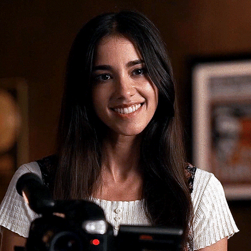 A Woman With Long Hair Is Smiling In Front Of A Camera . GIF