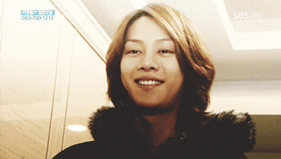 A Woman With Long Hair Is Smiling In Front Of A Sign That Says Sbs On It GIF