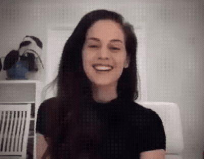 A Woman With Long Hair Is Smiling While Sitting In A Chair In A Room . GIF