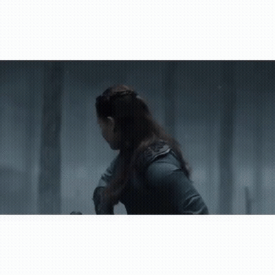 A Woman With Long Hair Is Standing In A Dark Forest With Trees In The Background . GIF