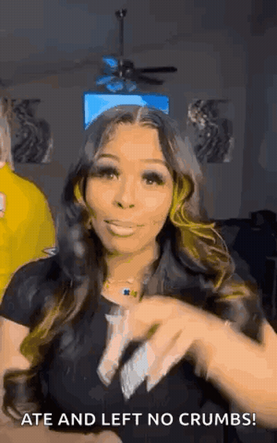 A Woman With Long Hair Is Standing In A Living Room With A Ceiling Fan In The Background . GIF