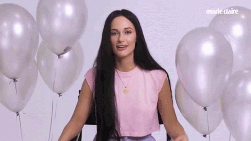 A Woman With Long Hair Is Standing In Front Of A Bunch Of Balloons . GIF