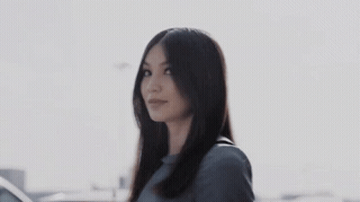 A Woman With Long Hair Is Standing In Front Of A Car And Smiling . GIF