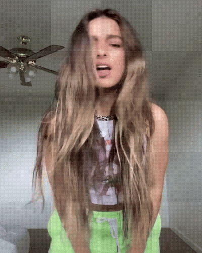 A Woman With Long Hair Is Standing In Front Of A Ceiling Fan And Sticking Out Her Tongue . GIF