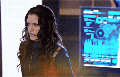 A Woman With Long Hair Is Standing In Front Of A Monitor That Says ' A ' On It . GIF
