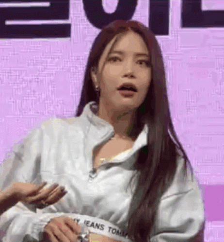 A Woman With Long Hair Is Standing In Front Of A Purple Background Wearing A White Jacket . GIF