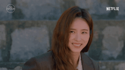 A Woman With Long Hair Is Standing In Front Of A Stone Wall . GIF