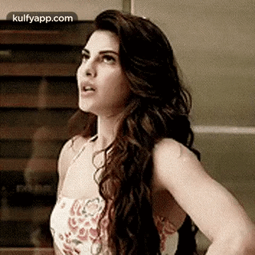 A Woman With Long Hair Is Standing In Front Of A Wall And Looking Up . GIF