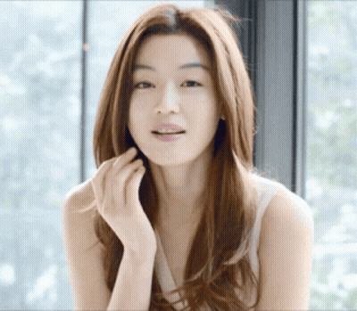 A Woman With Long Hair Is Standing In Front Of A Window GIF
