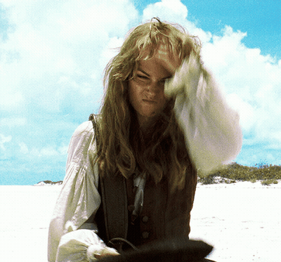 A Woman With Long Hair Is Standing On A Beach With Her Hand On Her Head GIF