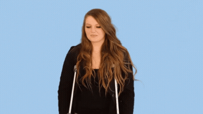 A Woman With Long Hair Is Standing With Crutches And Making A Funny Face . GIF