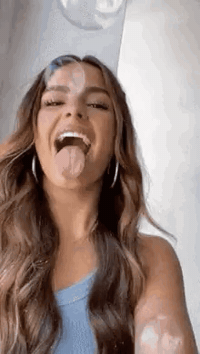 A Woman With Long Hair Is Sticking Her Tongue Out While Taking A Selfie . GIF