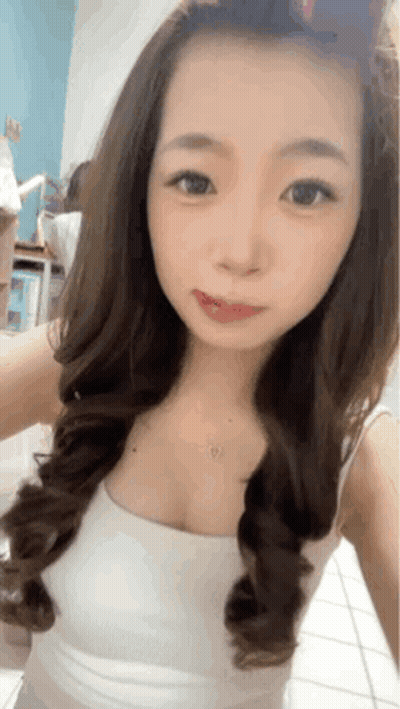 A Woman With Long Hair Is Taking A Selfie In A White Tank Top GIF