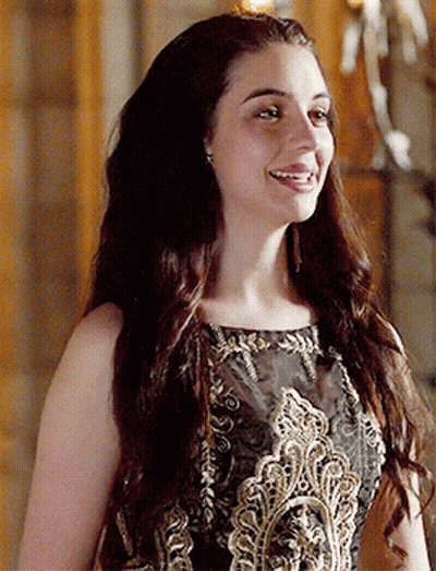 A Woman With Long Hair Is Wearing A Black And Gold Dress And Smiling GIF