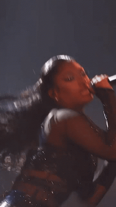 A Woman With Long Hair Is Wearing A Black Bodysuit With Rhinestones . GIF