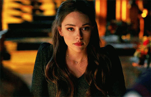 A Woman With Long Hair Is Wearing A Black Sweater And A Necklace . GIF