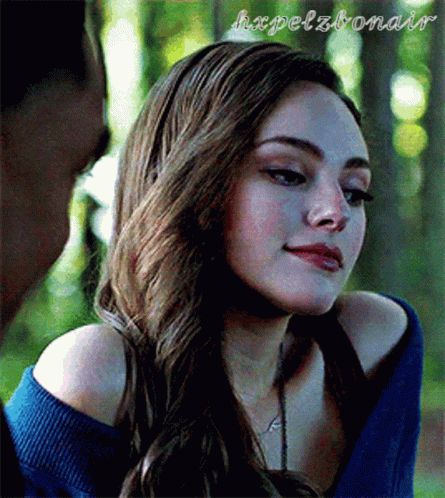 A Woman With Long Hair Is Wearing A Blue Sweater And A Necklace . GIF