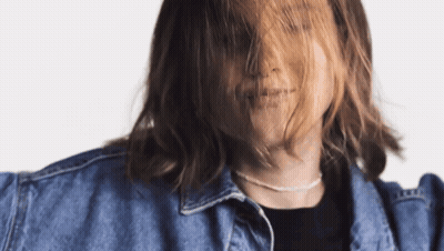 A Woman With Long Hair Is Wearing A Denim Jacket And A Necklace GIF