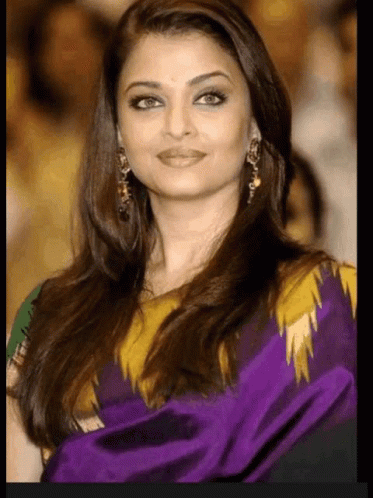 A Woman With Long Hair Is Wearing A Purple And Yellow Dress And Earrings . GIF