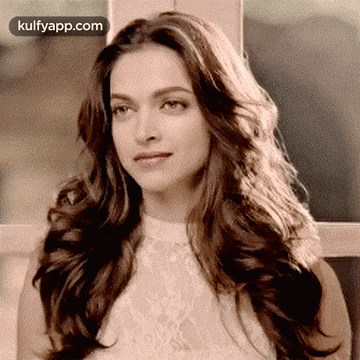 A Woman With Long Hair Is Wearing A White Top And Looking At The Camera . GIF