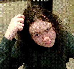 A Woman With Long Hair Scratches Her Head In Front Of A Punching Bag That Says ' Boxing ' On It GIF