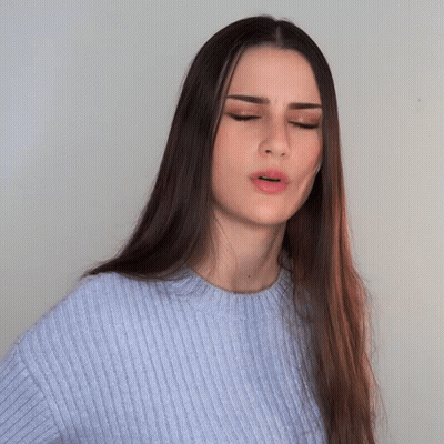 A Woman With Long Hair Wearing A Blue Sweater Is Making A Funny Face GIF