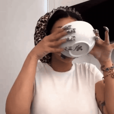 A Woman With Long Nails Is Drinking From A Bowl With A Logo On It . GIF