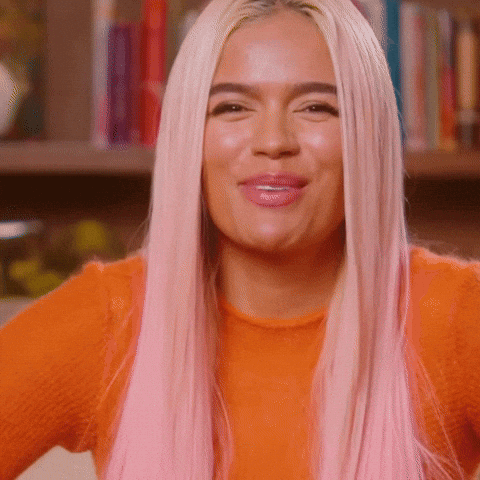 A Woman With Long Pink Hair Is Wearing An Orange Sweater And Smiling . GIF