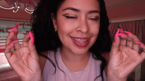 A Woman With Long Pink Nails And Braces On Her Teeth Smiles GIF