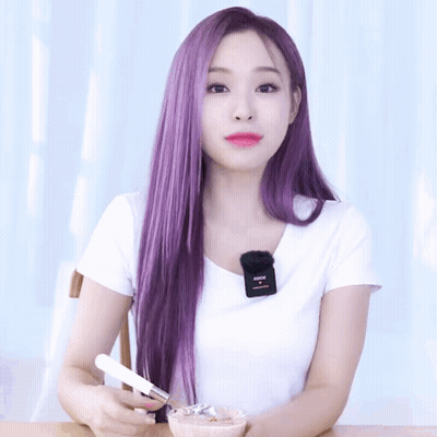 A Woman With Long Purple Hair Is Wearing A White Shirt With A Microphone On Her Neck GIF
