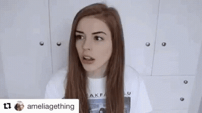 A Woman With Long Red Hair Is Making A Funny Face While Wearing A White Shirt . GIF
