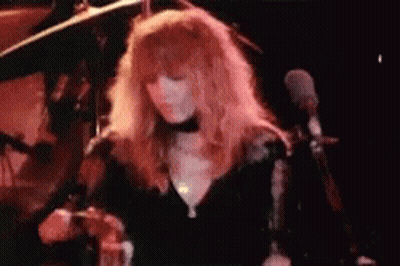 A Woman With Long Red Hair Is Singing Into A Microphone On Stage . GIF