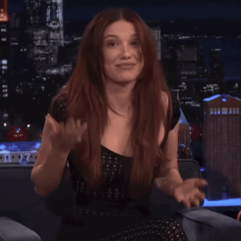 A Woman With Long Red Hair Is Sitting In Front Of A City Skyline GIF