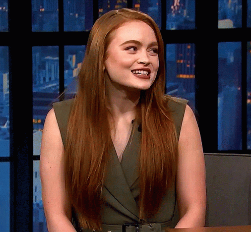 A Woman With Long Red Hair Is Smiling And Wearing A Green Dress GIF